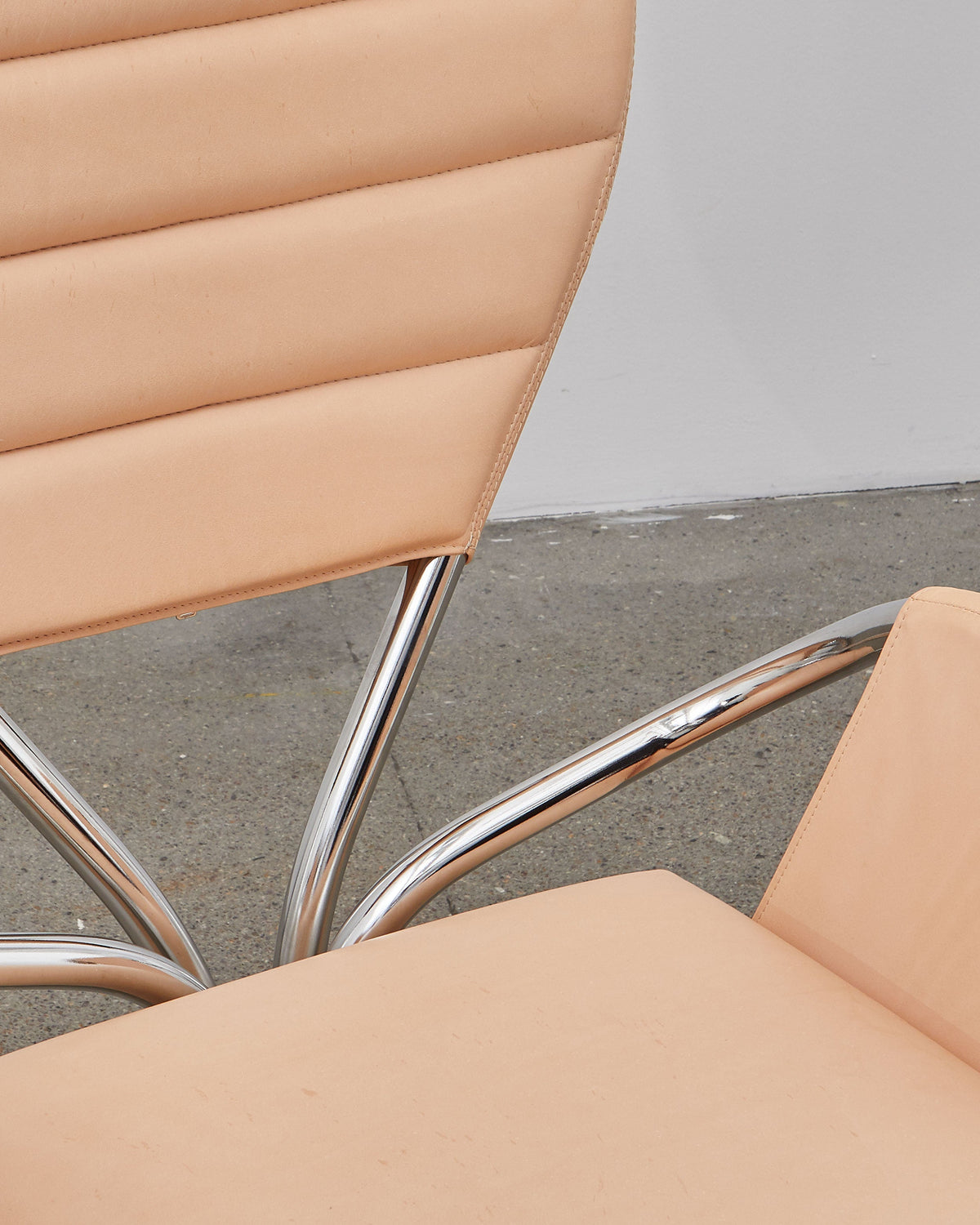 A beige leather upholstered chair with a chrome-plated steel frame and a rounded backrest, designed in a modernist style.