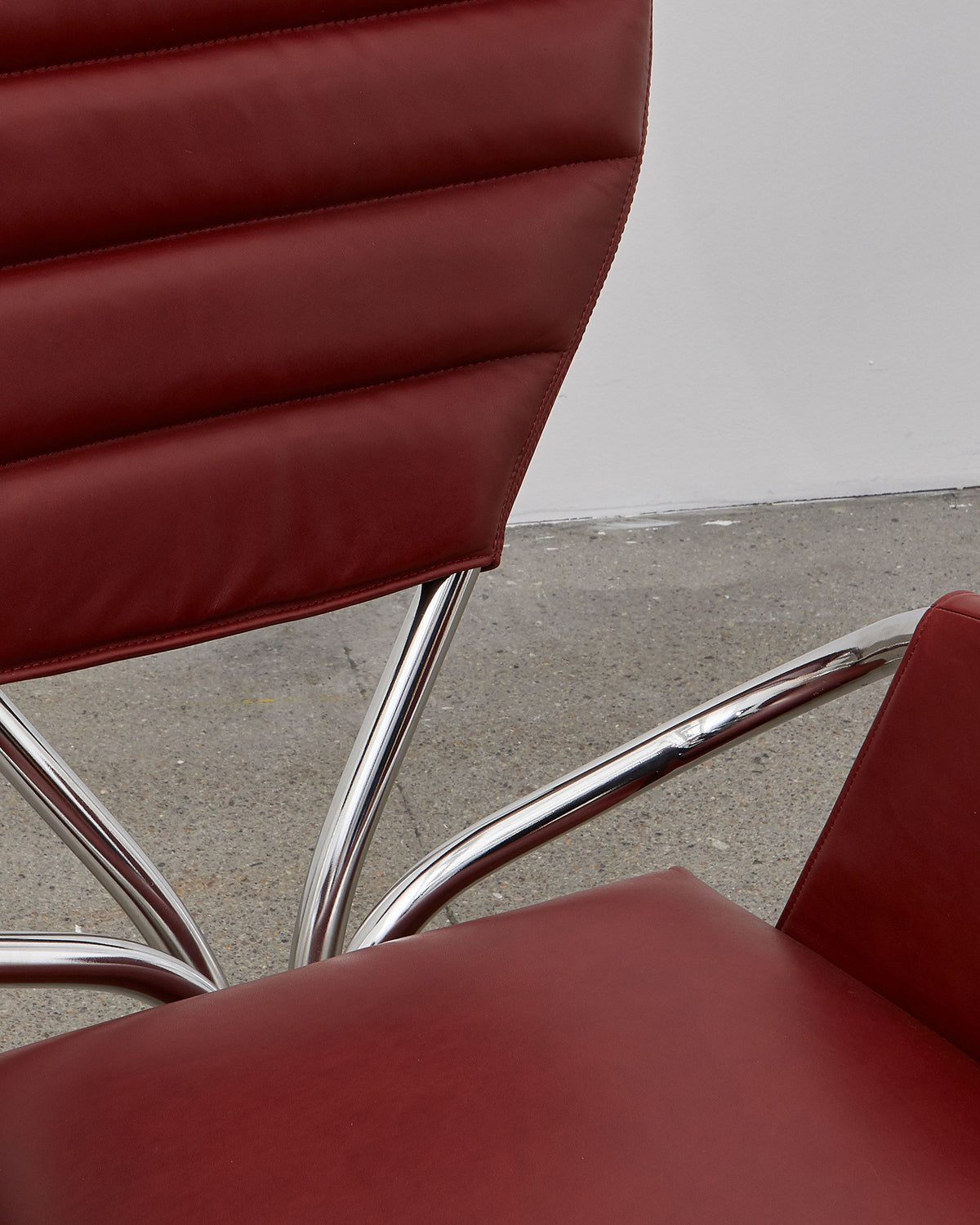 A red leather upholstered chair with a chrome-plated steel frame and a rounded backrest, designed in a modernist style.