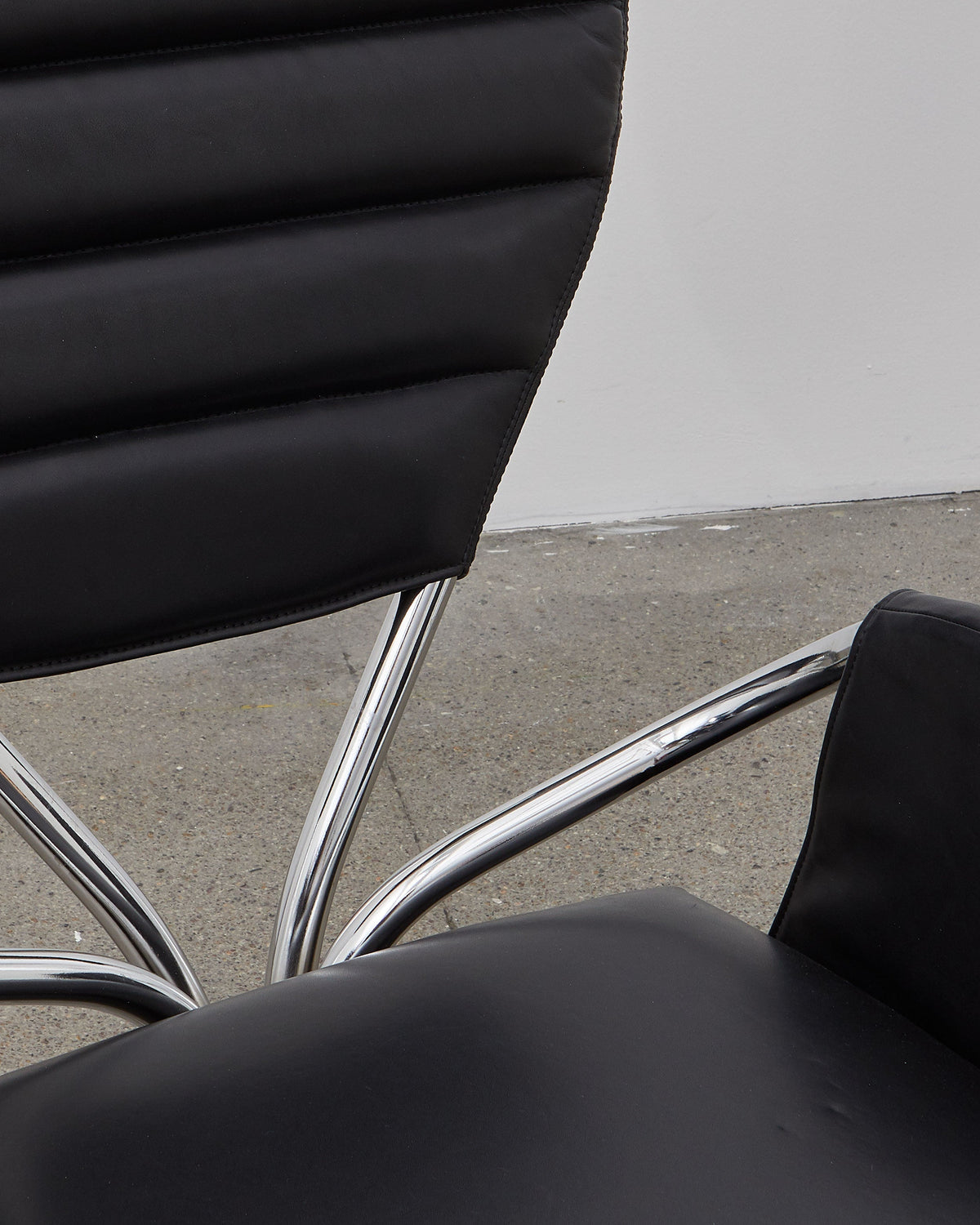 A black leather upholstered chair with a chrome-plated steel frame and a rounded backrest, designed in a modernist style.