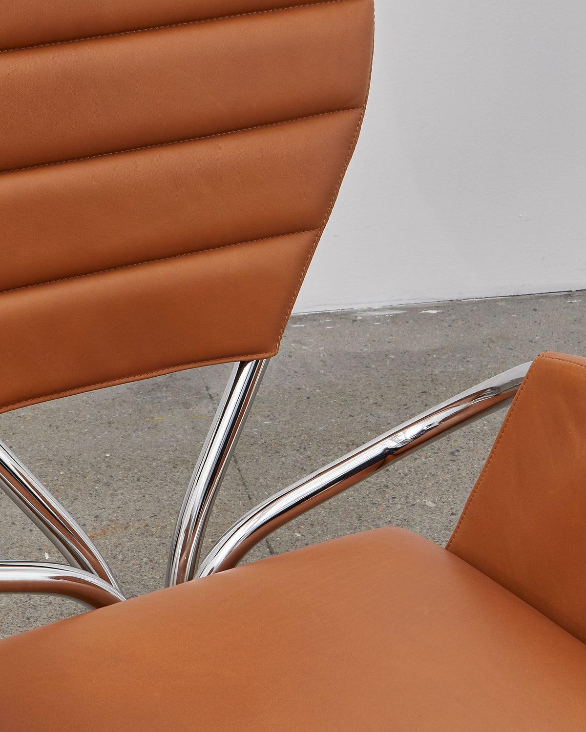 A walnut brown leather upholstered chair with a chrome-plated steel frame and a rounded backrest, designed in a modernist style.