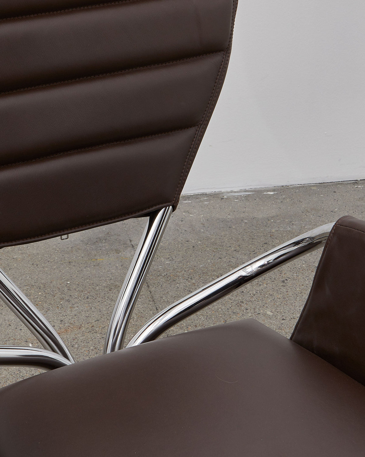 A brown leather upholstered chair with a chrome-plated steel frame and a rounded backrest, designed in a modernist style.