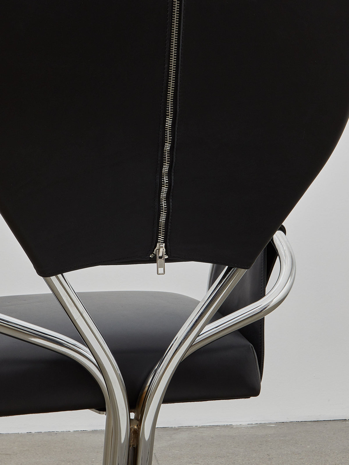 A black leather upholstered chair with a chrome-plated steel frame and a rounded backrest, designed in a modernist style.