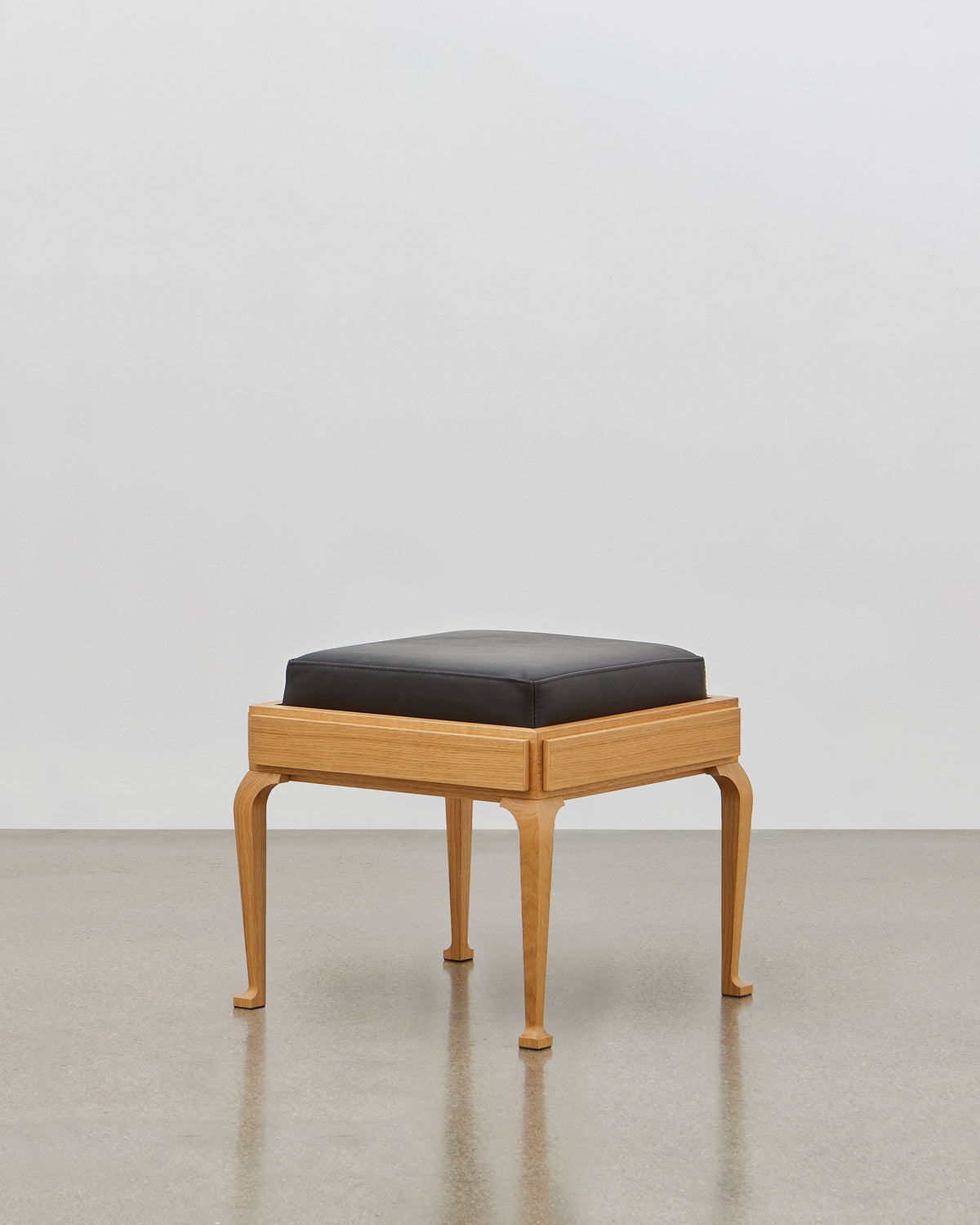 PH Stool by Poul Henningsen, Danish design classic (1920) A black upholstered stool standing on four angled wooden legs.