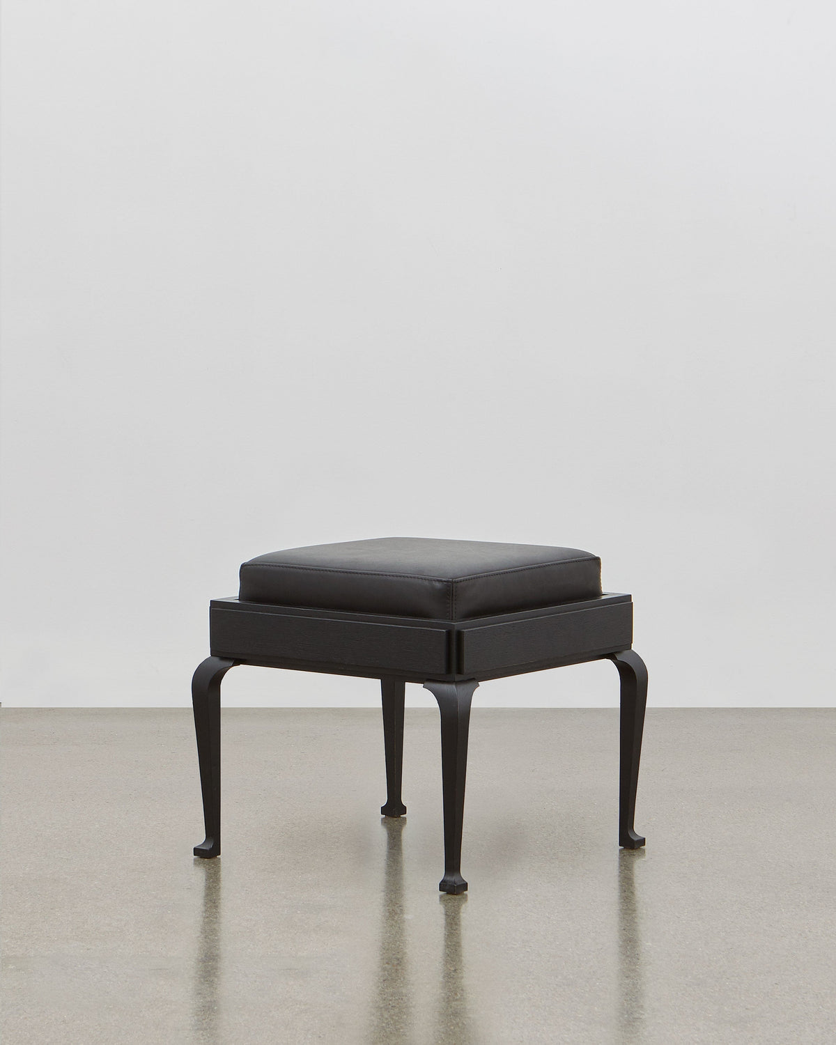 PH Stool by Poul Henningsen, Danish design classic (1920) A black upholstered stool standing on four angled wooden legs.