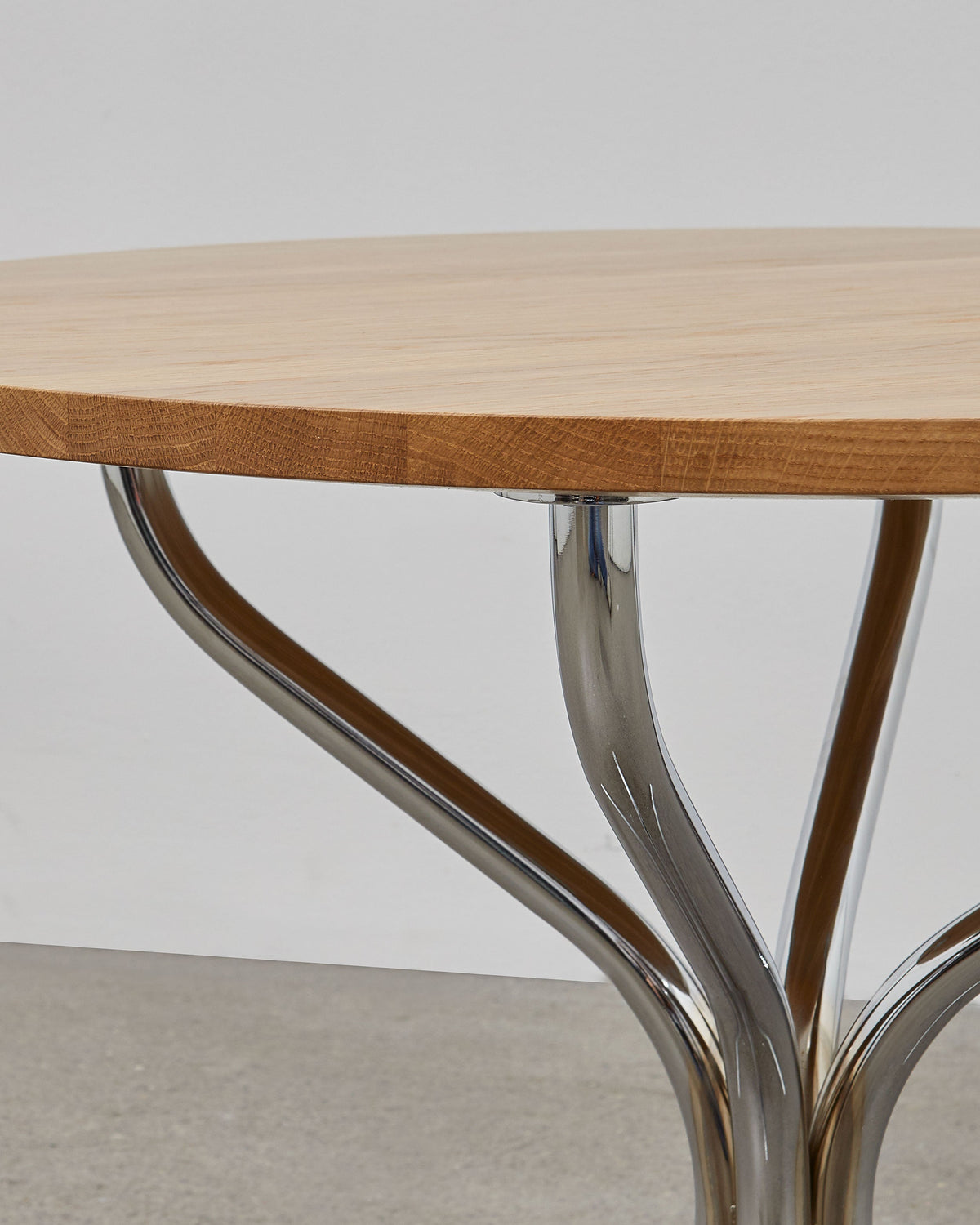 A round wooden lounge table with chrome metal legs, designed by Poul Henningsen.