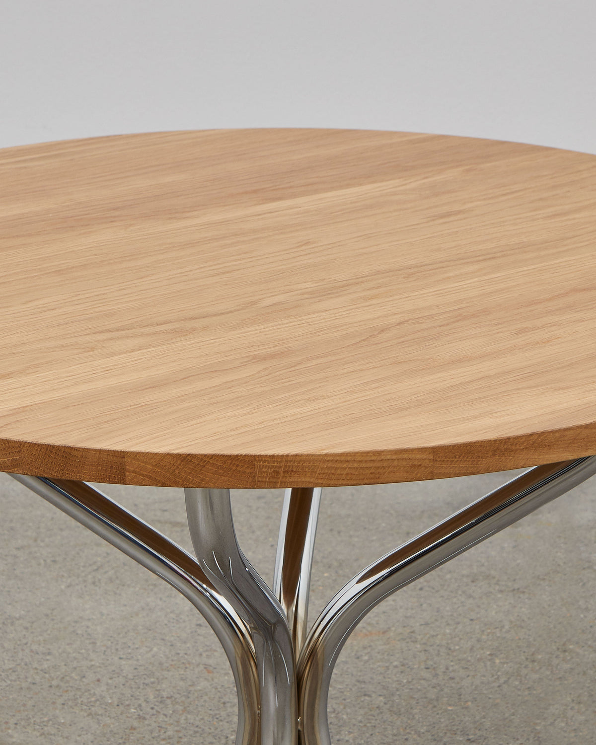 A round wooden lounge table with chrome metal legs, designed by Poul Henningsen.