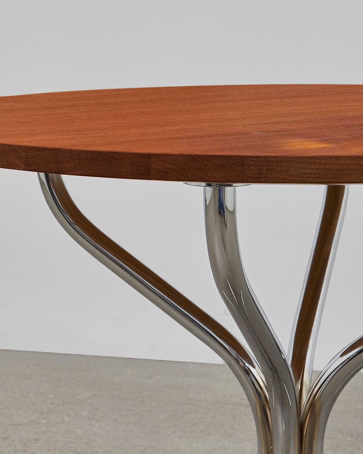 A round wooden lounge table with chrome metal legs, designed by Poul Henningsen.